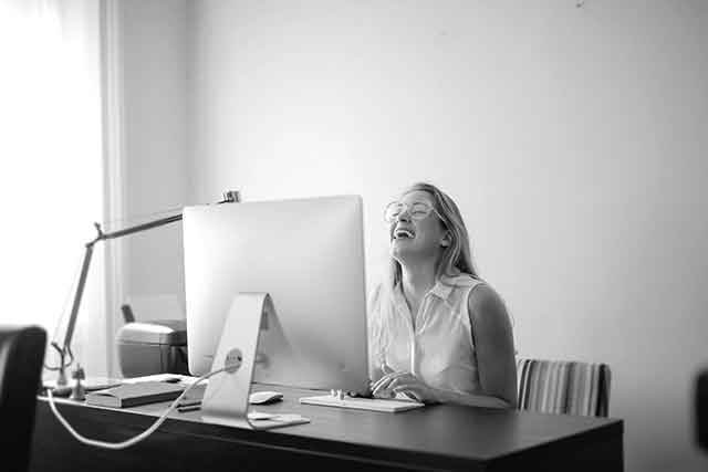 using humor at work woman laughing at computer